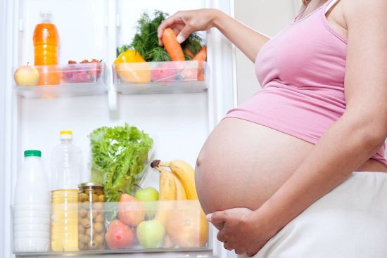 Беременная берет овощи из холодильника