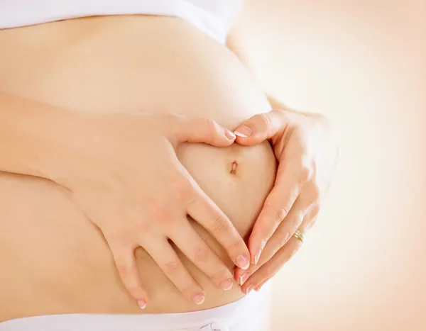 Беременная женщина, взявшись за руки в форме сердца на ее ремуо младенца — стоковое фото