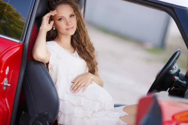Беременные брюнетка девочка и ее красный автомобиль — стоковое фото