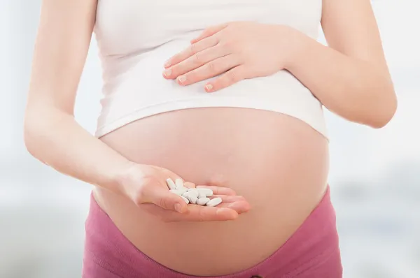 Живота беременной женщины и витамин таблетки в руке — стоковое фото