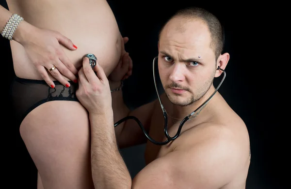 Отец, слушая его жена беременная живот с stethescope — стоковое фото