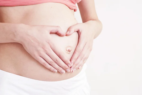 Женщина держит руки в форме сердца на живот беременной — стоковое фото