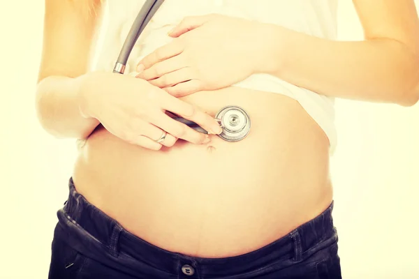 Беременная женщина со стетоскопом, слушая ее ребенок — стоковое фото