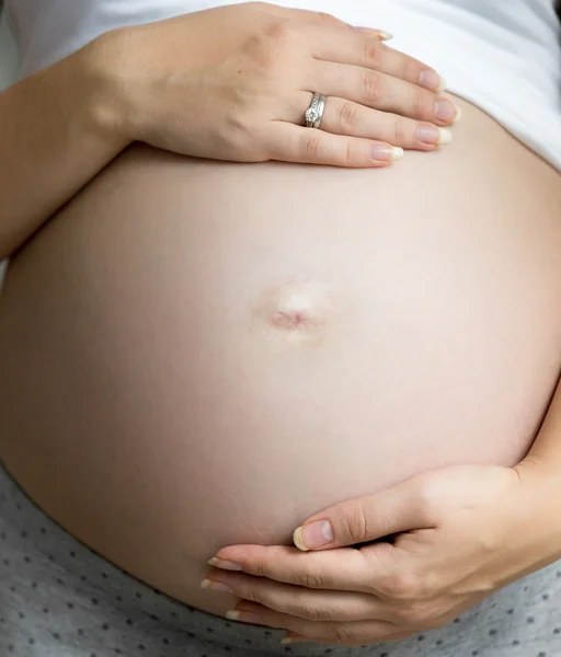 Крупным планом беременной женщины, взявшись за руки на большой живот — стоковое фото