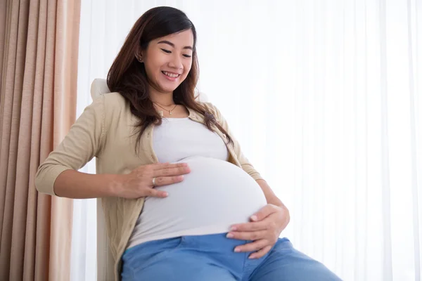Счастливый беременная женщина Азии касаясь ее большой живот, сидя — стоковое фото