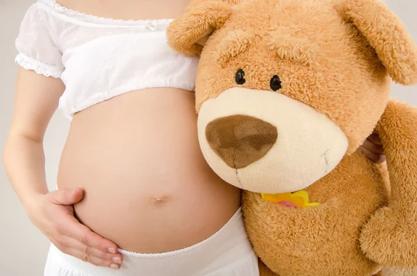 Крупным планом на беременный живот и большой плюшевый медведь — стоковое фото