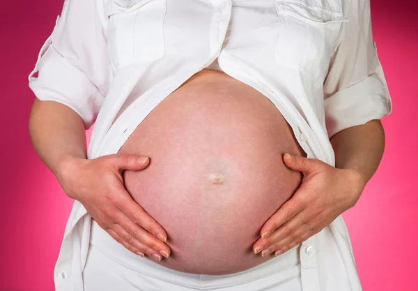 Беременная женщина поглаживая живот руками на розовом фоне — стоковое фото