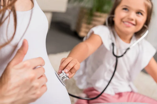Девушка, слушая беременный живот через стетоскоп — стоковое фото