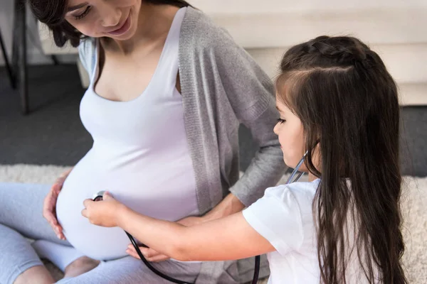 Девушка, слушая беременный живот через стетоскоп — стоковое фото