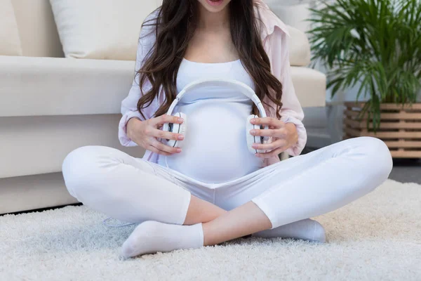 Беременная женщина, держащая наушники над живот — стоковое фото