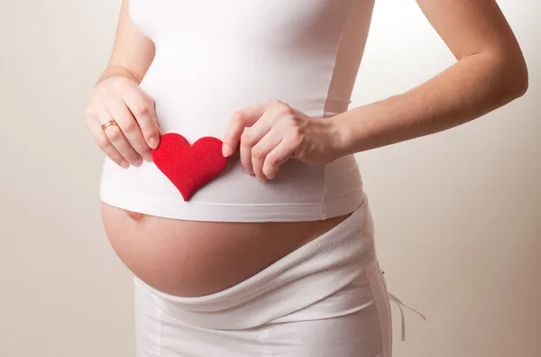 Беременная женщина, положил сердце игрушка — стоковое фото